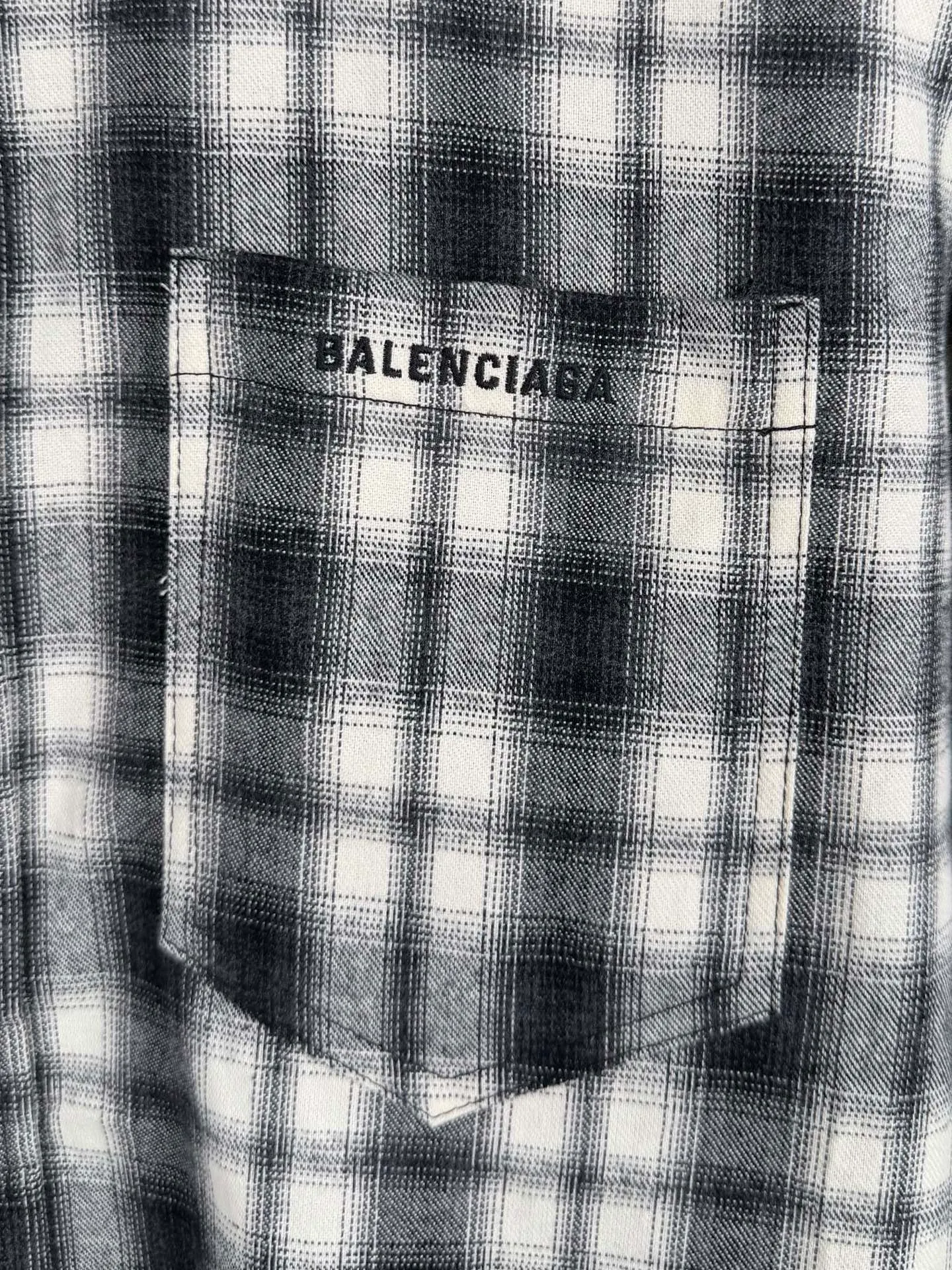 BALENCIAGA/balenciaga Black White plaid pocket embroidered logo shirt jacket The technical difficulties of this plaid shirt focus on fabric finishing, plaid matching and component sewing details. The fabric has been sanded and distressed to create a fine velvet feel on the surface, changing the original luster of the fabric and making the Black and White plaid colors transition softly. At the same time, the drape properties of the fabric itself are retained, taking into account the looseness of the upper body and the silhouette of the body, without appearing soft and shapeless. The biggest test of plaid garments comes from the alignment of the pieces. The front and rear body, large and small sleeves, and chest pockets are all independent pieces. In the cutting stage, the horizontal and vertical axes of the plaid need to be aligned, and the external chest bag is cut separately. The plaid on the bag surface needs to form a visual coordination with the main body of the garment. Cutting and typesetting will produce additional fabric loss, and there are high requirements for the cutting accuracy of the cutting bed typesetting and workers. The collar adopts a double-layer combined structure, and the collar surface and collar seat are double-stitched with even and regular stitching spacing to ensure the lapel's long-lasting shape and resistance to warping and deformation after repeated bending. The placket is sewn with regular topstitching and paired with Black matte buttons. The button points need to be aligned with the checkered lines to avoid damaging the overall visual order. The splicing of the cuffs also takes into account the grain direction, and the overlocking process reinforces the seams to improve the durability of the garment. After the entire garment is sewn, it also undergoes a garment washing process to further strengthen the Retro texture of the fabric, unify the tone and texture of the entire garment, weaken the harshness of industrial production, and finally present a relaxed Retro garment effect. Size: 46 48 50 52